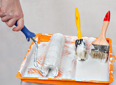 Hands painter dunks roller brush in tray of white paint.